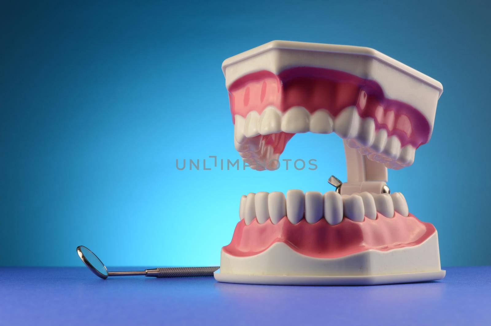 A display of dental teeth and a professional mouth mirror over blue for dentist purposes.