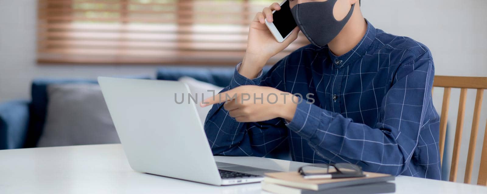 Young asian business man in face mask talking smartphone and work on laptop computer for protect covid-19, businessman quarantine work from home with notebook, social distancing and stay home.