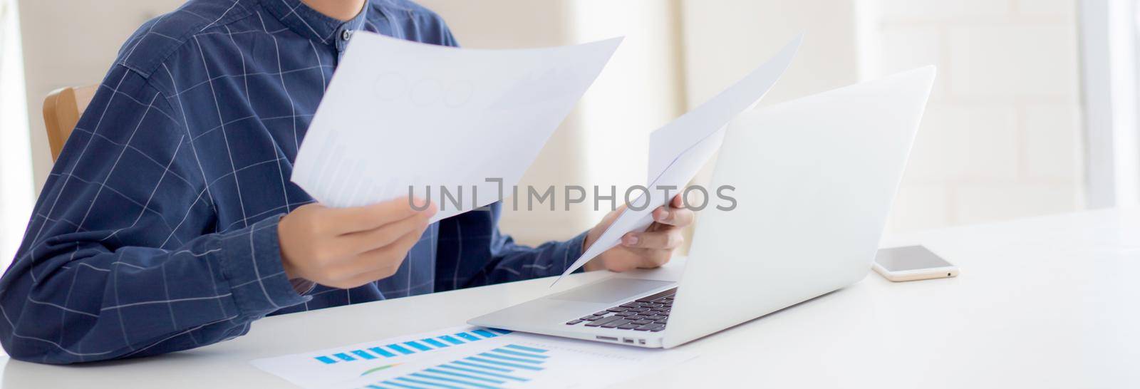 Young asian business man looking document data graph and chart paper, marketing and investment, report of statistics profit for financial, economic and growth of finance, management and planning.