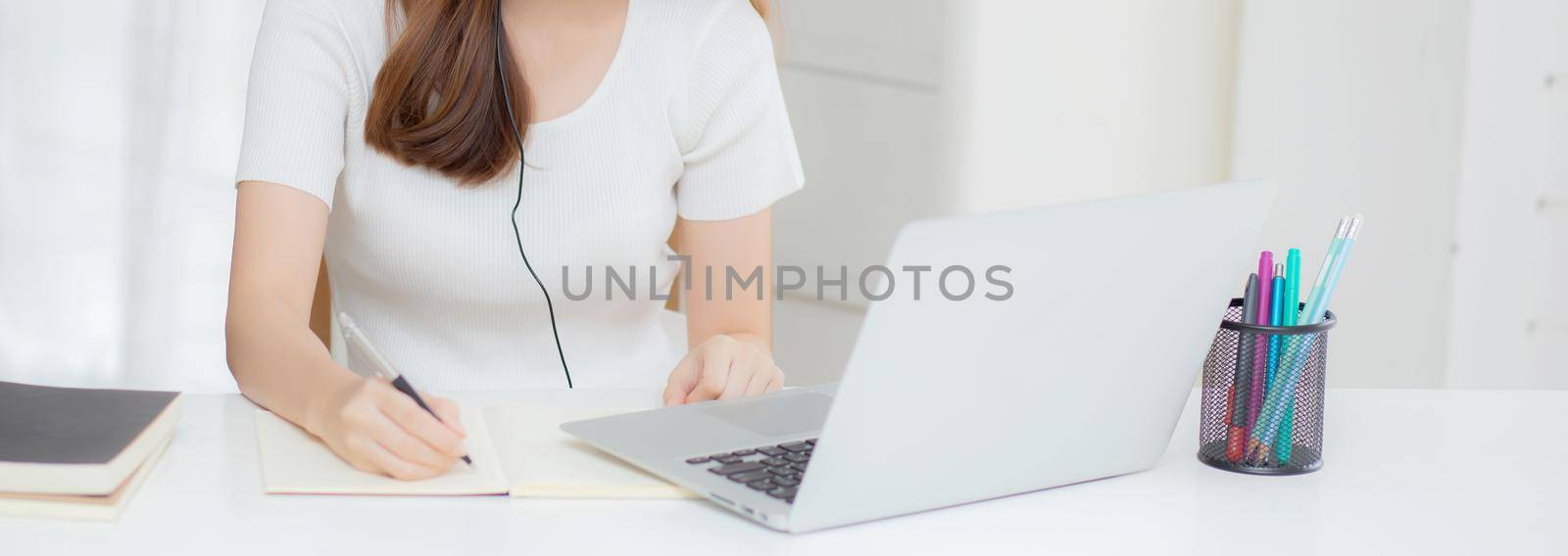 Young asian woman wearing headphone study online with e-learning on desk, girl wearing headset learning to internet with laptop computer at home, new normal, distance education and training. by nnudoo