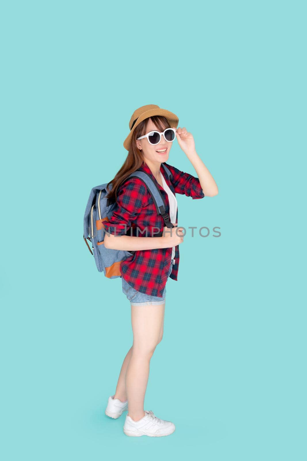 Beautiful portrait young asian woman wear sunglasses and hat smile excited and confident enjoy summer trip holiday isolated blue background, girl cheerful having backpack in vacation, travel concept.