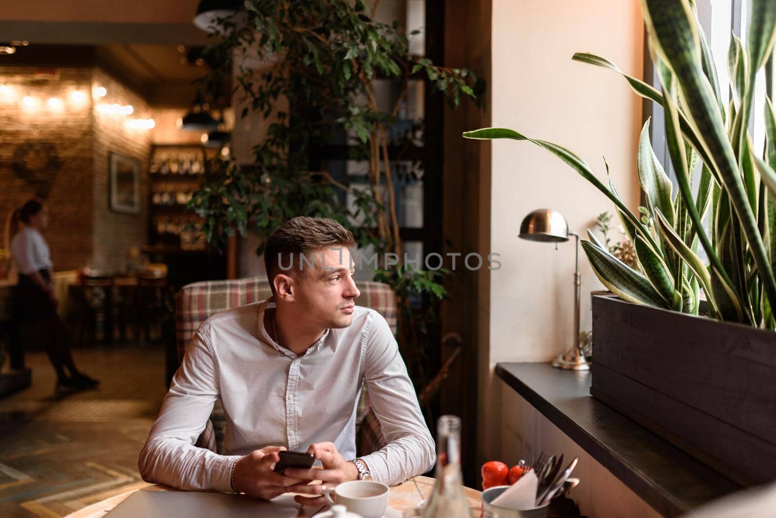 Waist up of guy sitting at the table while holding smartphone in coffee shop. Modern lifestyle concept