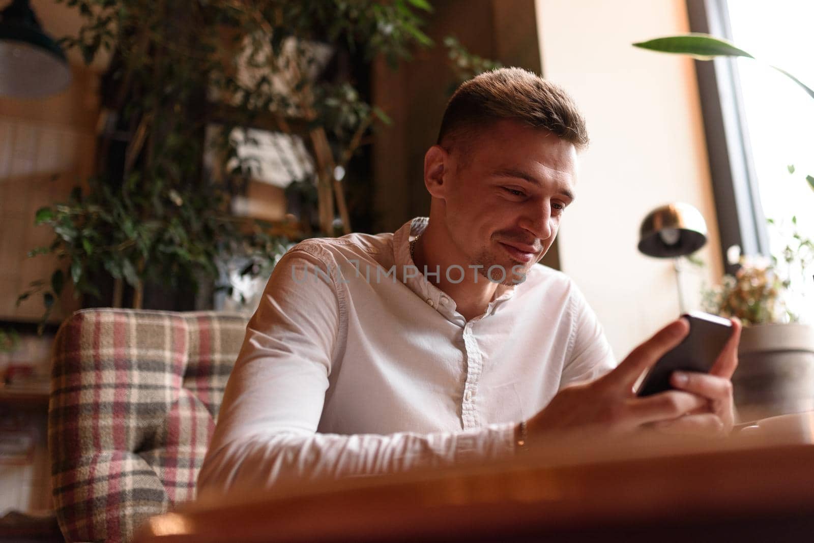 Happy Caucasian guy looking at the smartphone screen while having coffee at coffee shop. Modern lifestyle concept