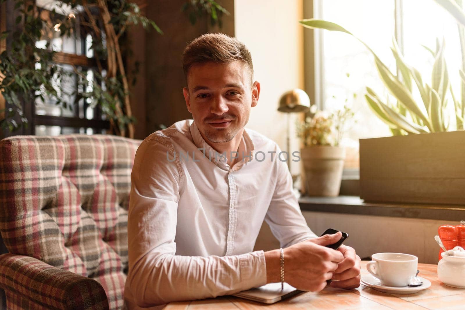 Waist up of smiling handsome guy wearing white shirt while sitting in cafe and having coffee. Lifestyle concept