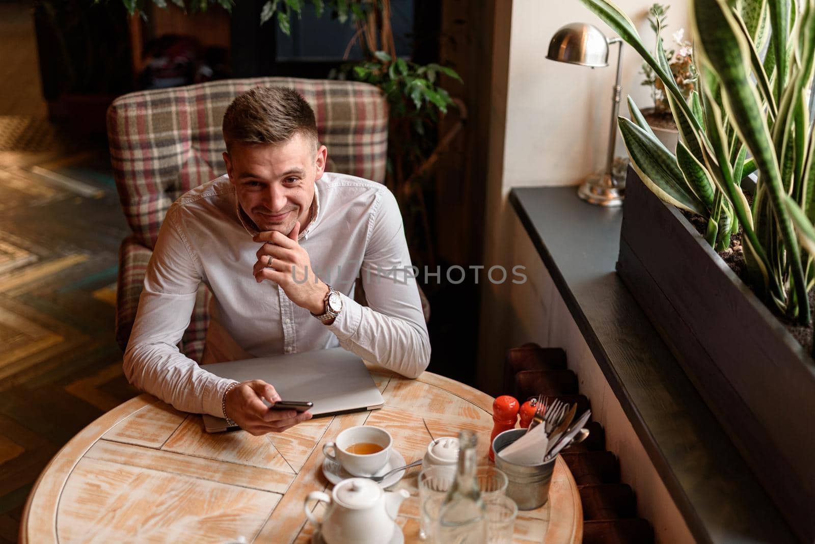 Top view of happy young businessman using smartphone while sitting at the table in cafe. Lifestyle concept