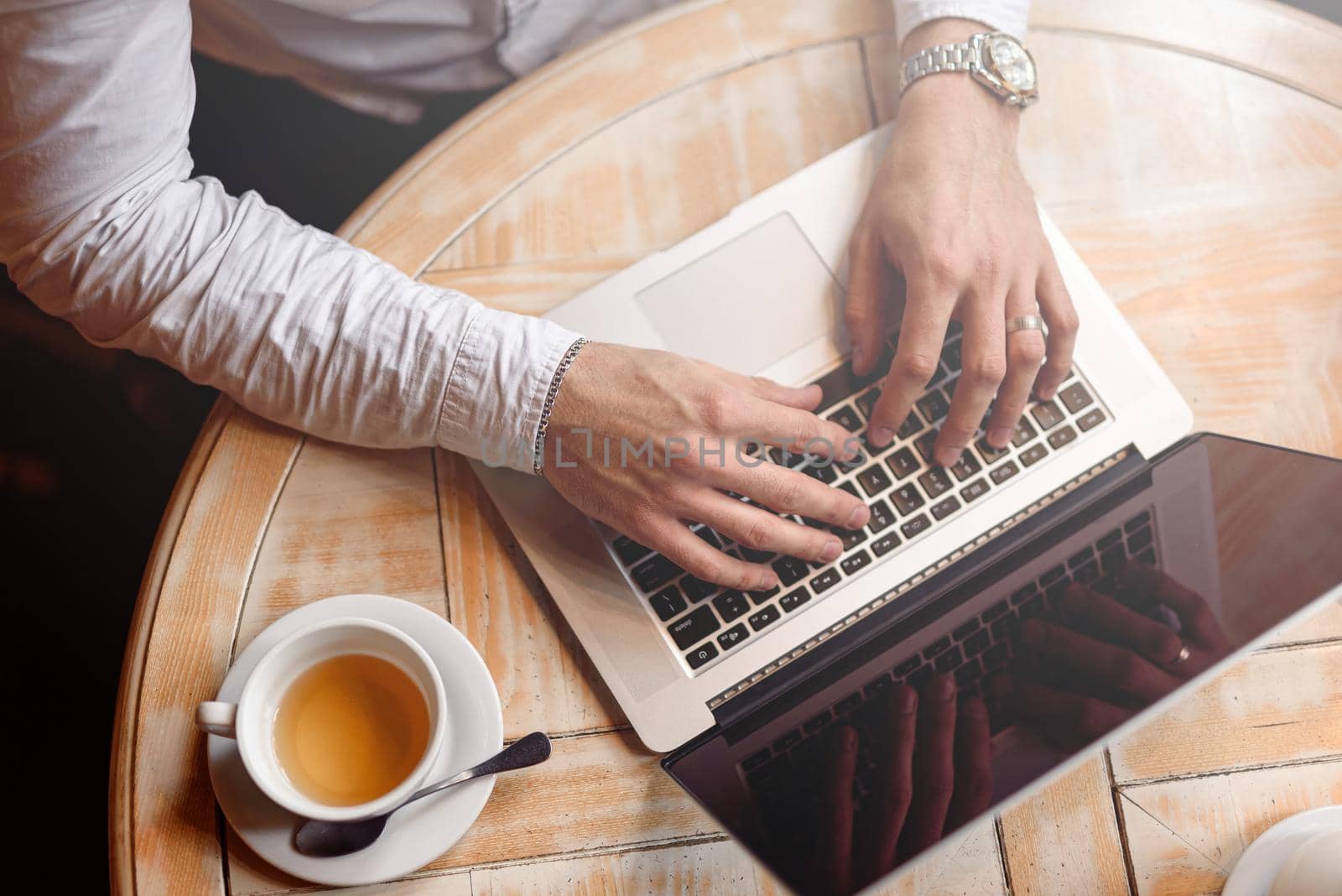 Top view of male hands typing on laptop while enjoying tea. Selective focus. Lifestyle concept