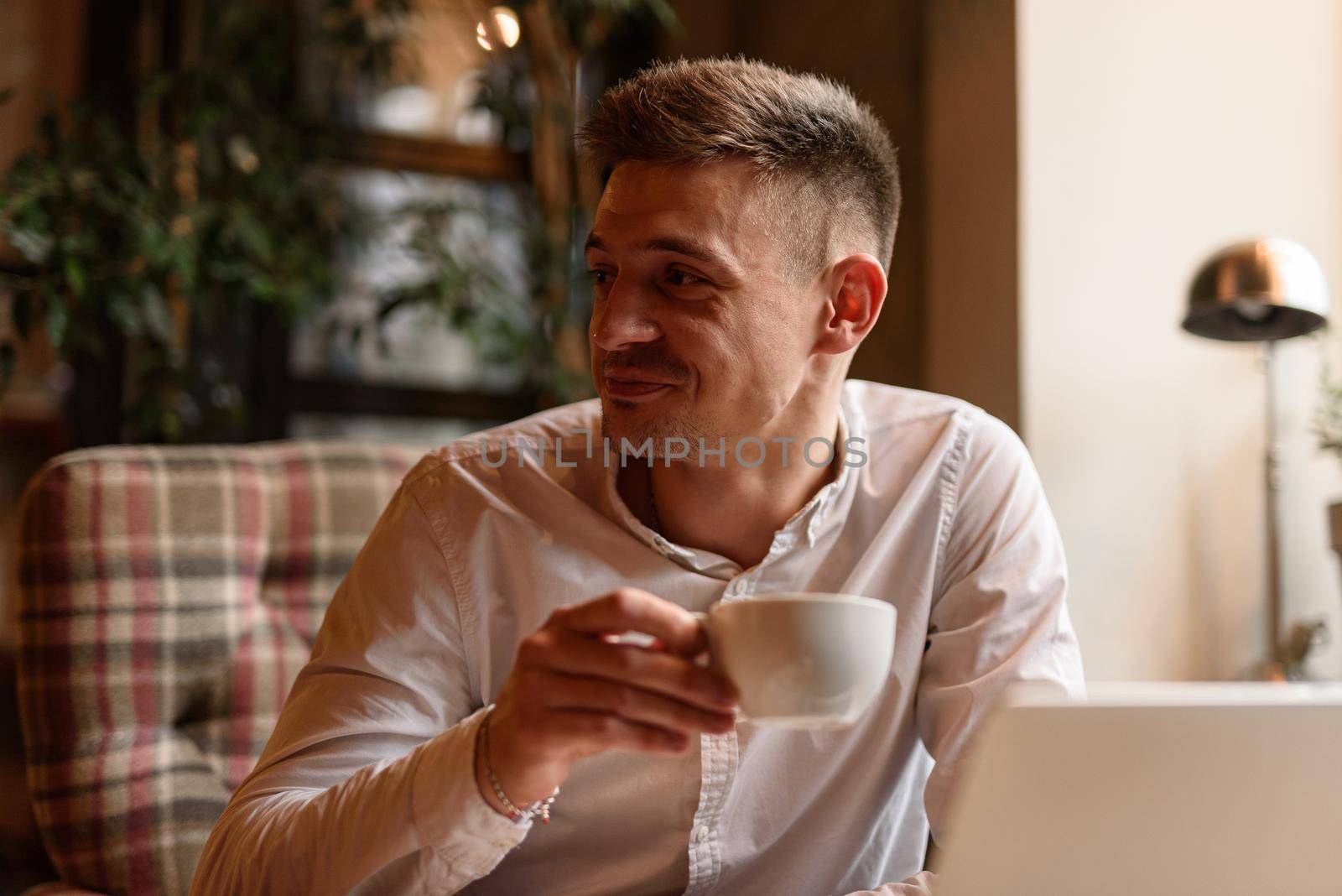 Portrait of smiling handsome guy enjoying tea while working with laptop in coffee shop. Lifestyle concept