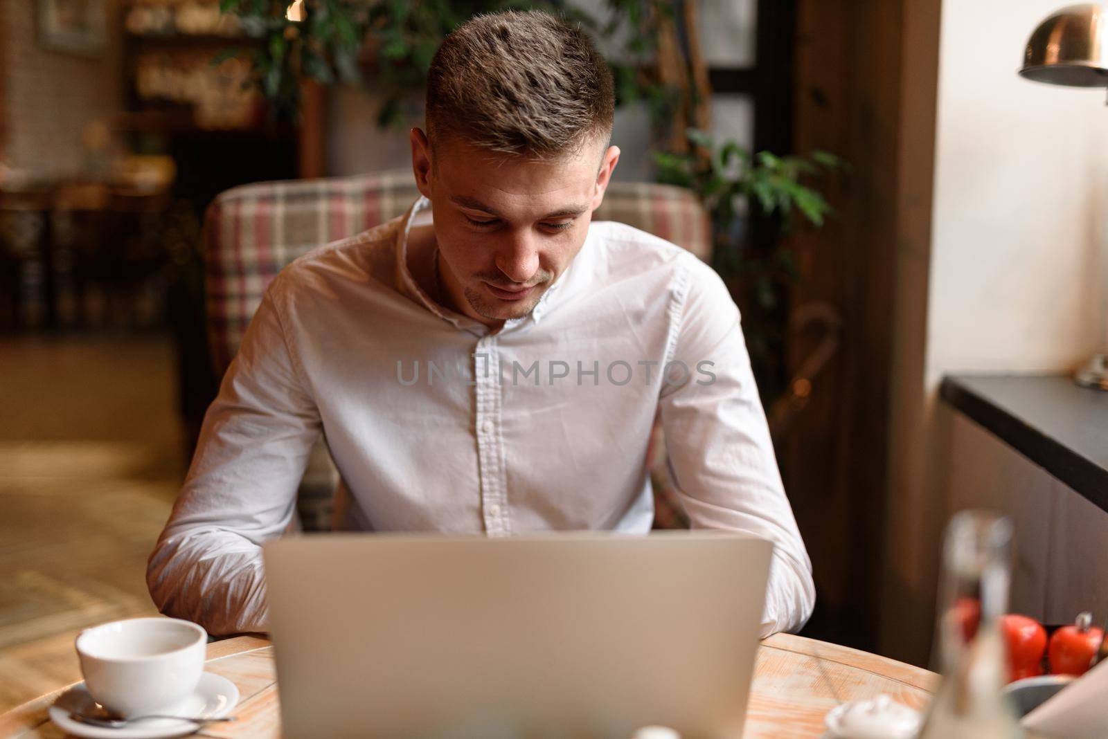 Portrait of young Caucasian man in casual shirt using laptop computer at cafe while having lunch. Lifestyle concept