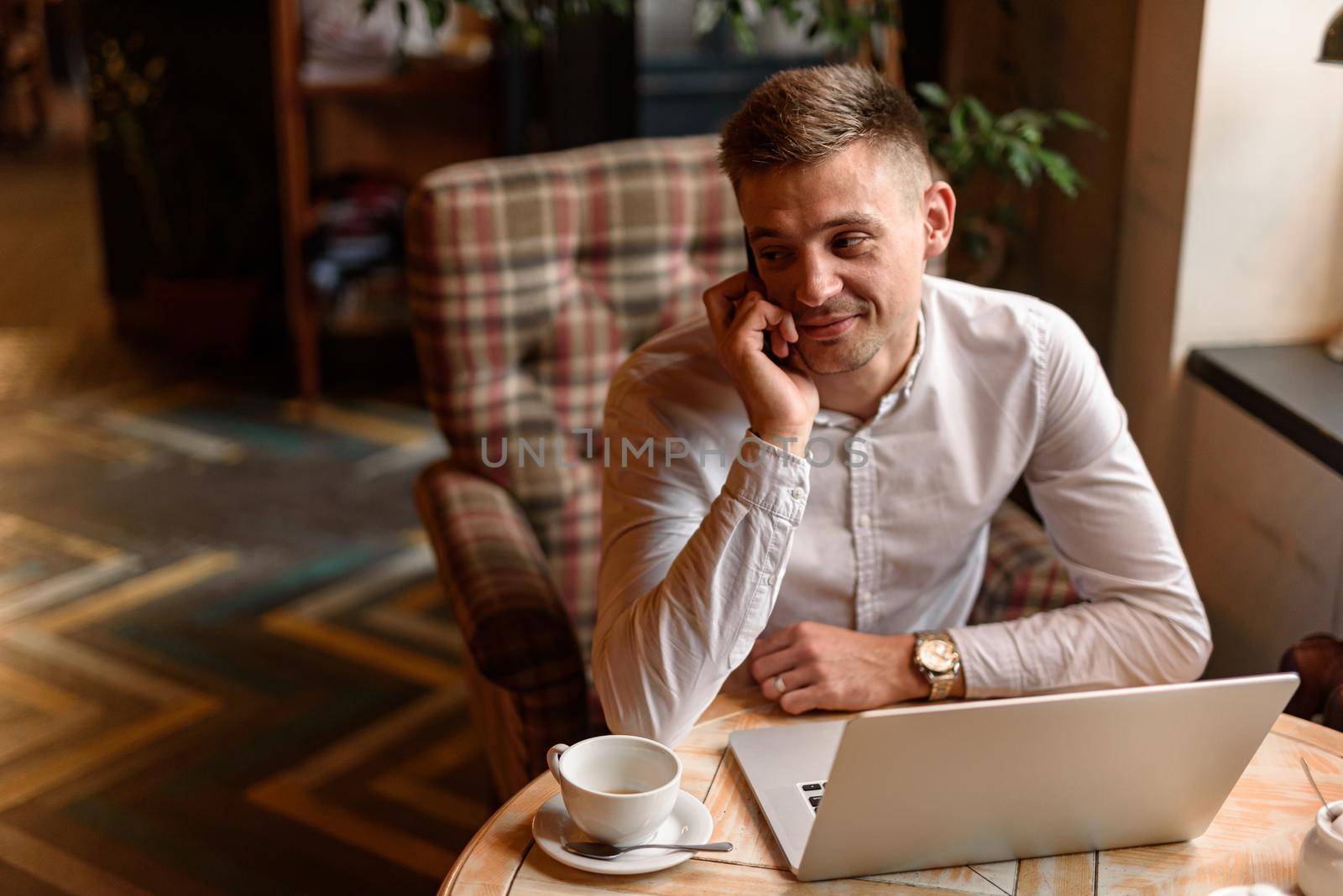 Happy young man working with laptop while talking on his mobile phone during coffee break. Lifestyle concept