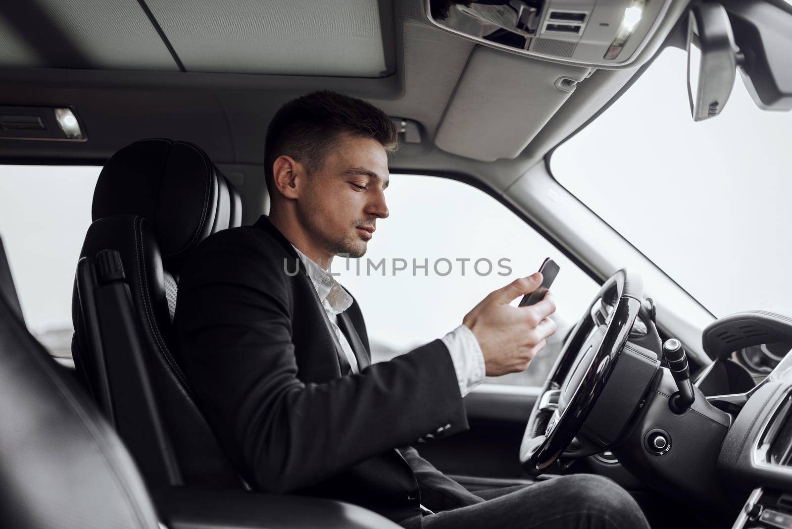 Confident young man working on his smartphone while sitting in the car. Rent and trade-in concept