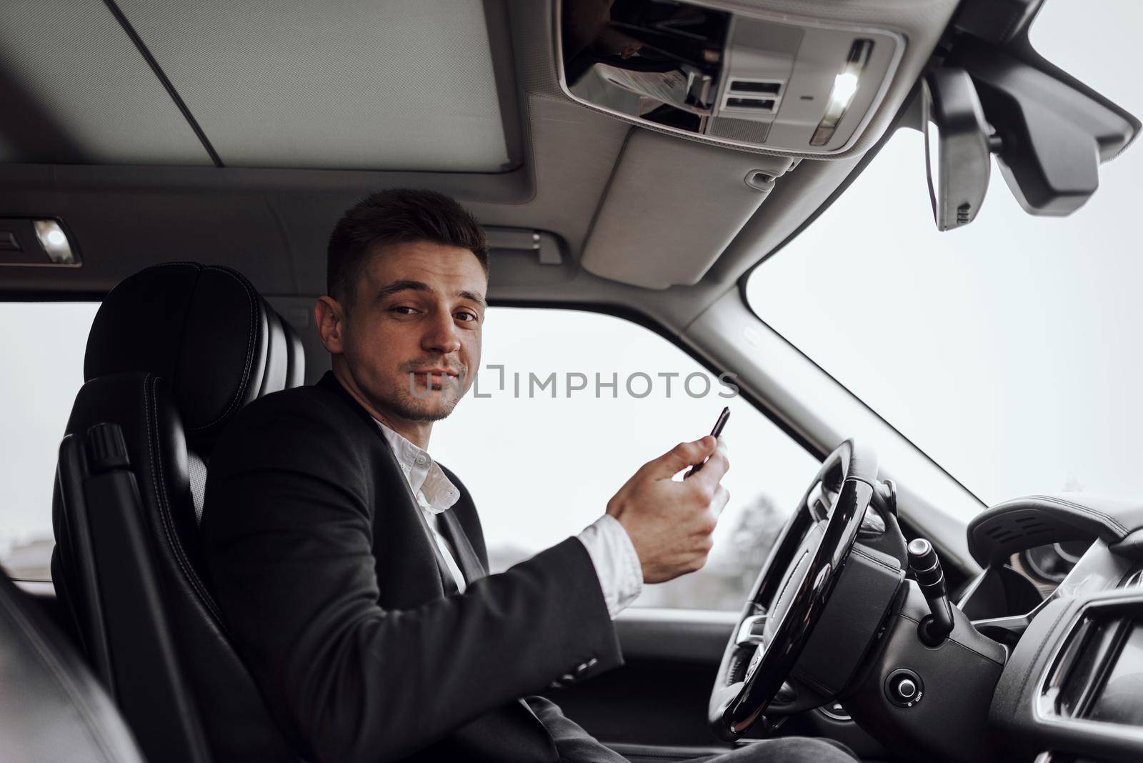 Portrait of smiling young man holding smartphone while driving car. Rent and trade-in concept