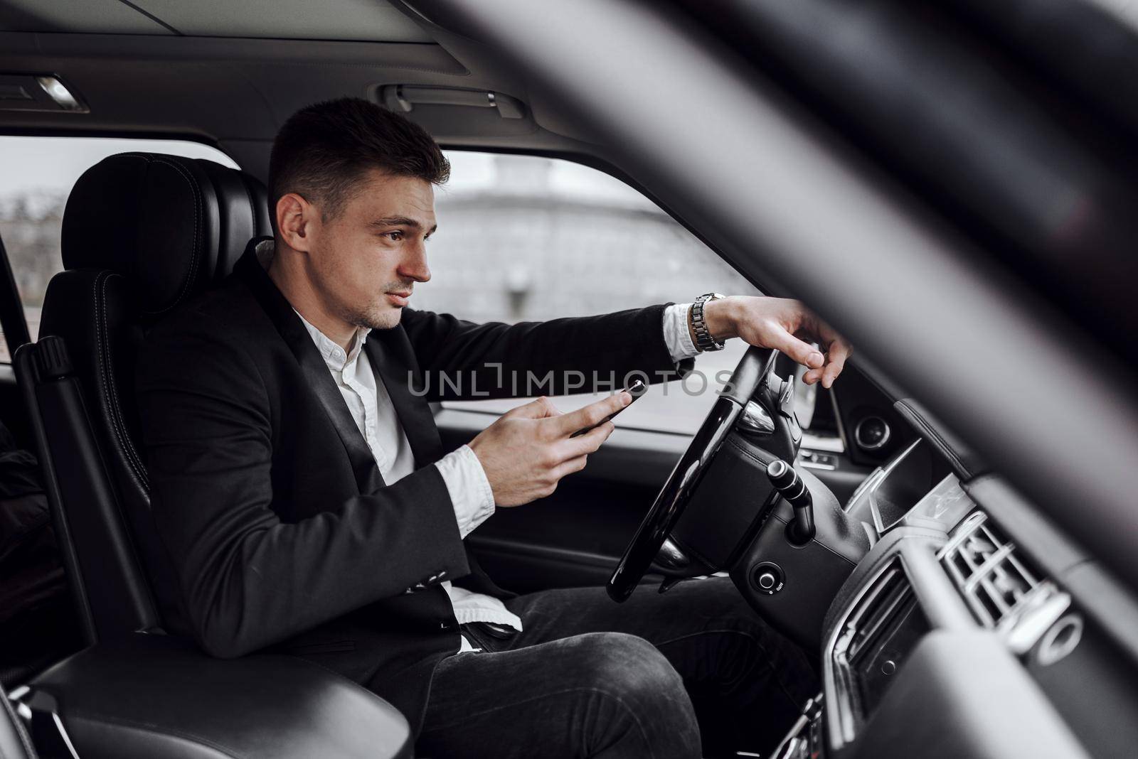 Side view of happy young businessman looking at smartphone screen in rented car. Rent and trade-in concept