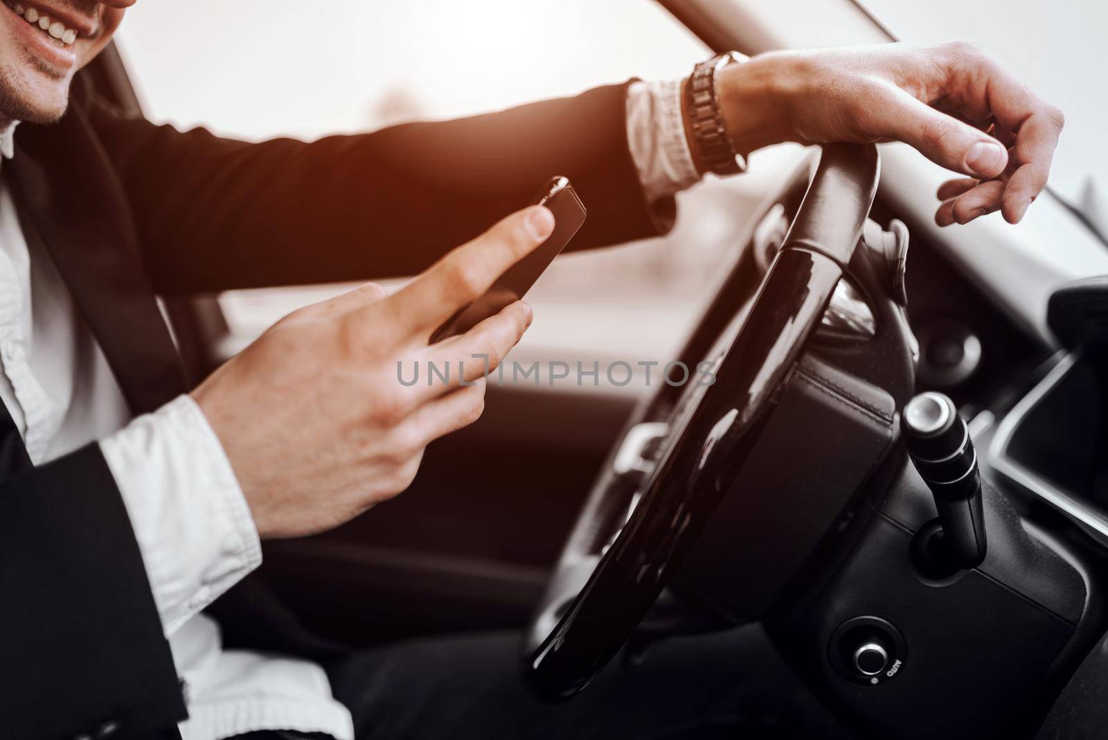 Close up of happy businessman typing message while sitting in automobile. Rent and trade-in concept