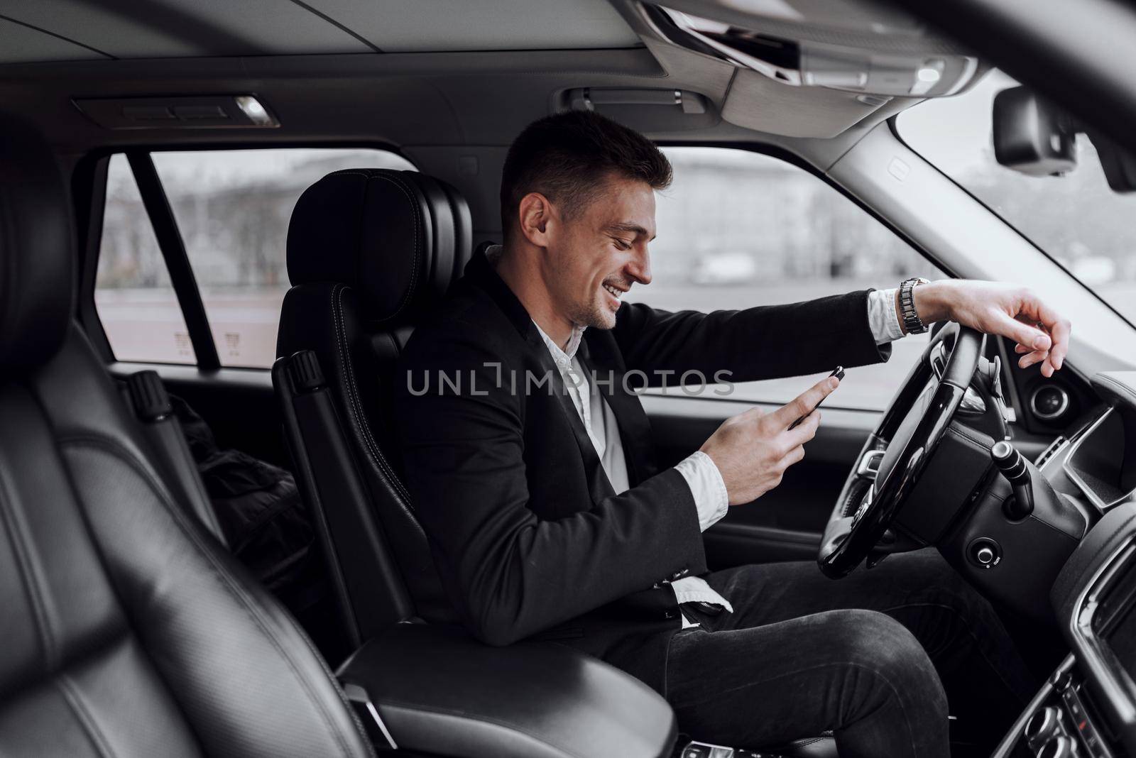 Smiling young man typing message in car by monakoartstudio