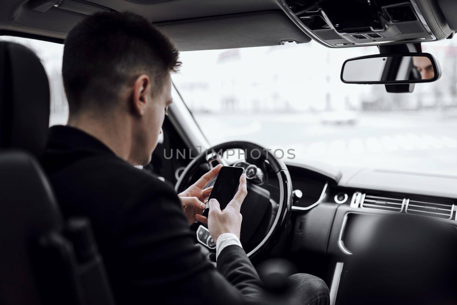 Back view of young businessman looking at smartphone screen while sitting in car. Rent and trade-in concept