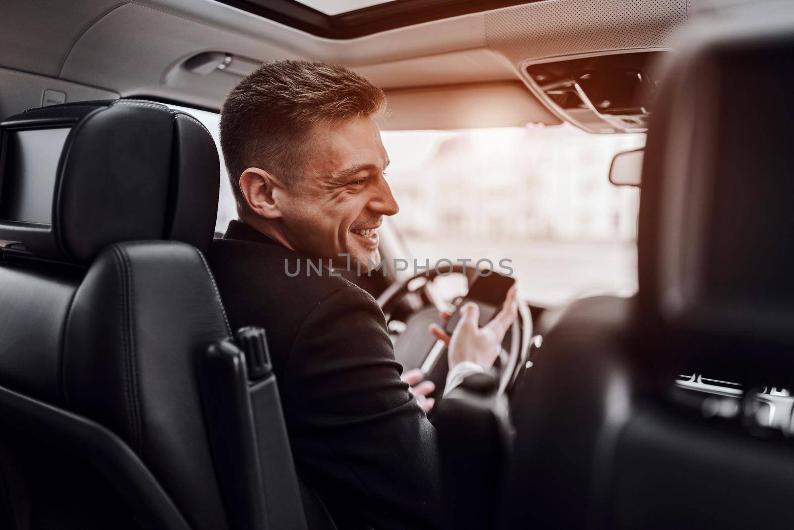 Smiling young man holding mobile phone in car by monakoartstudio