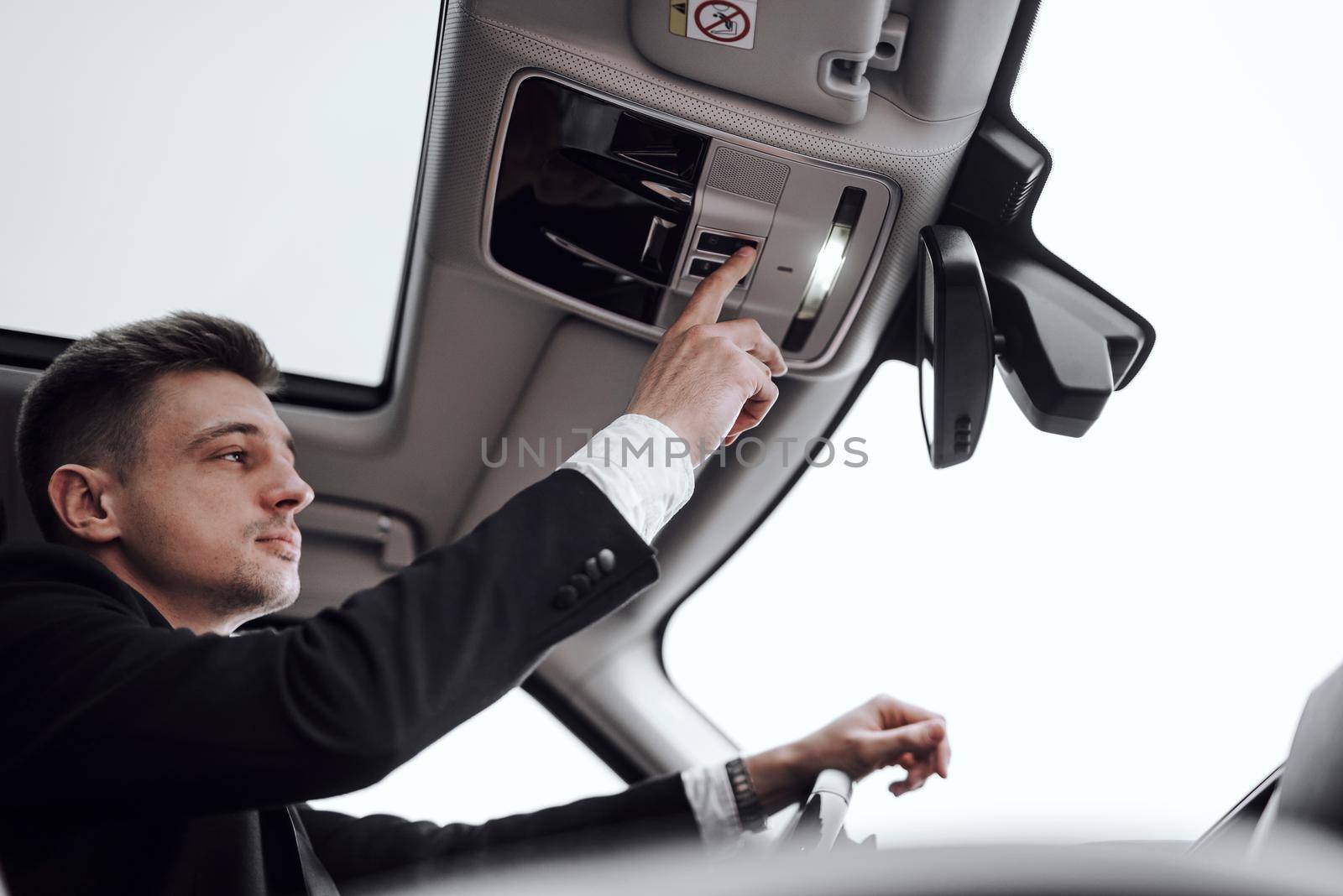 Confident young businessman sitting in car while turning on the light. Rent and trade-in concept