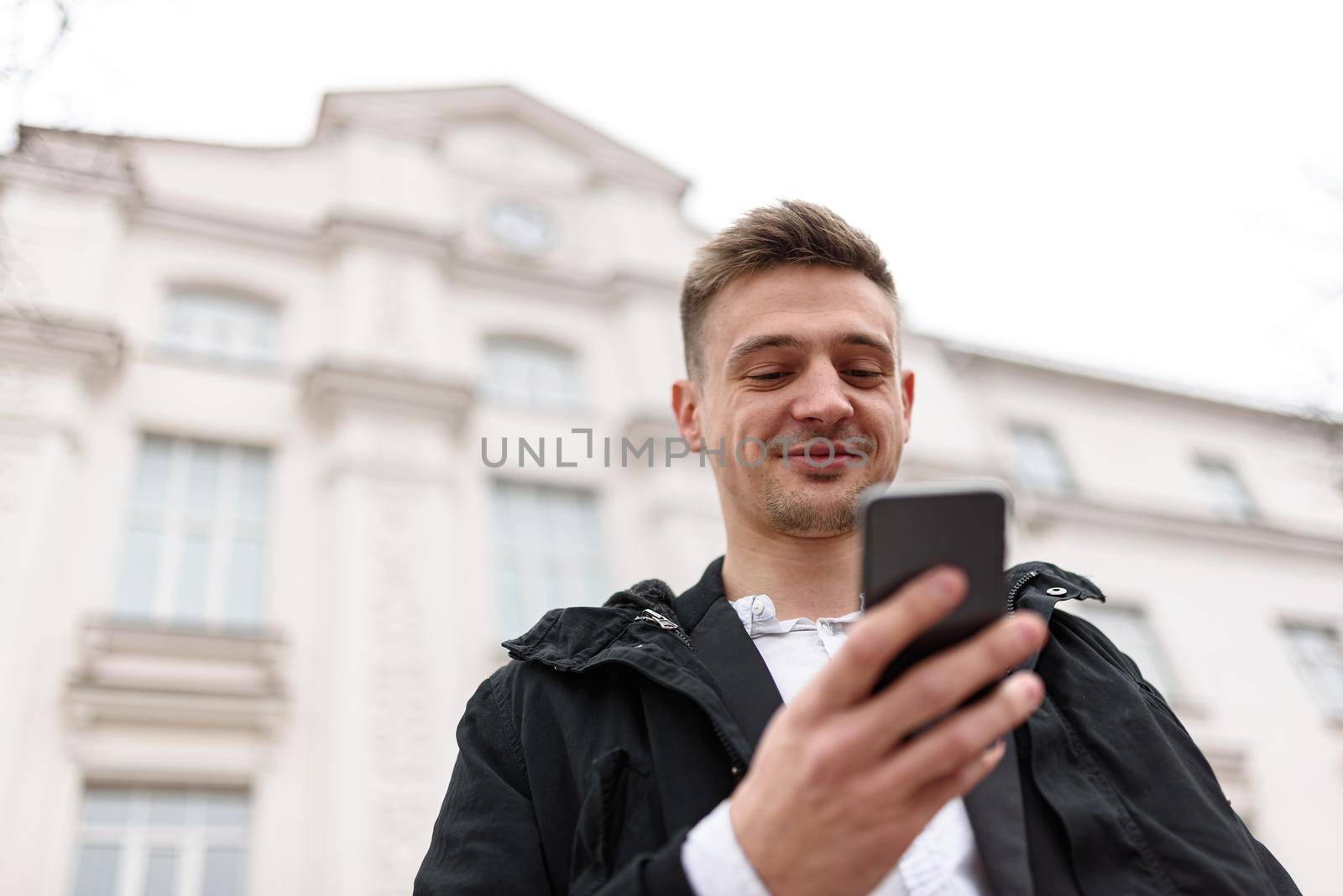 Happy young man sending a message on smartphone outdoors. Copy space. Lifestyle concept