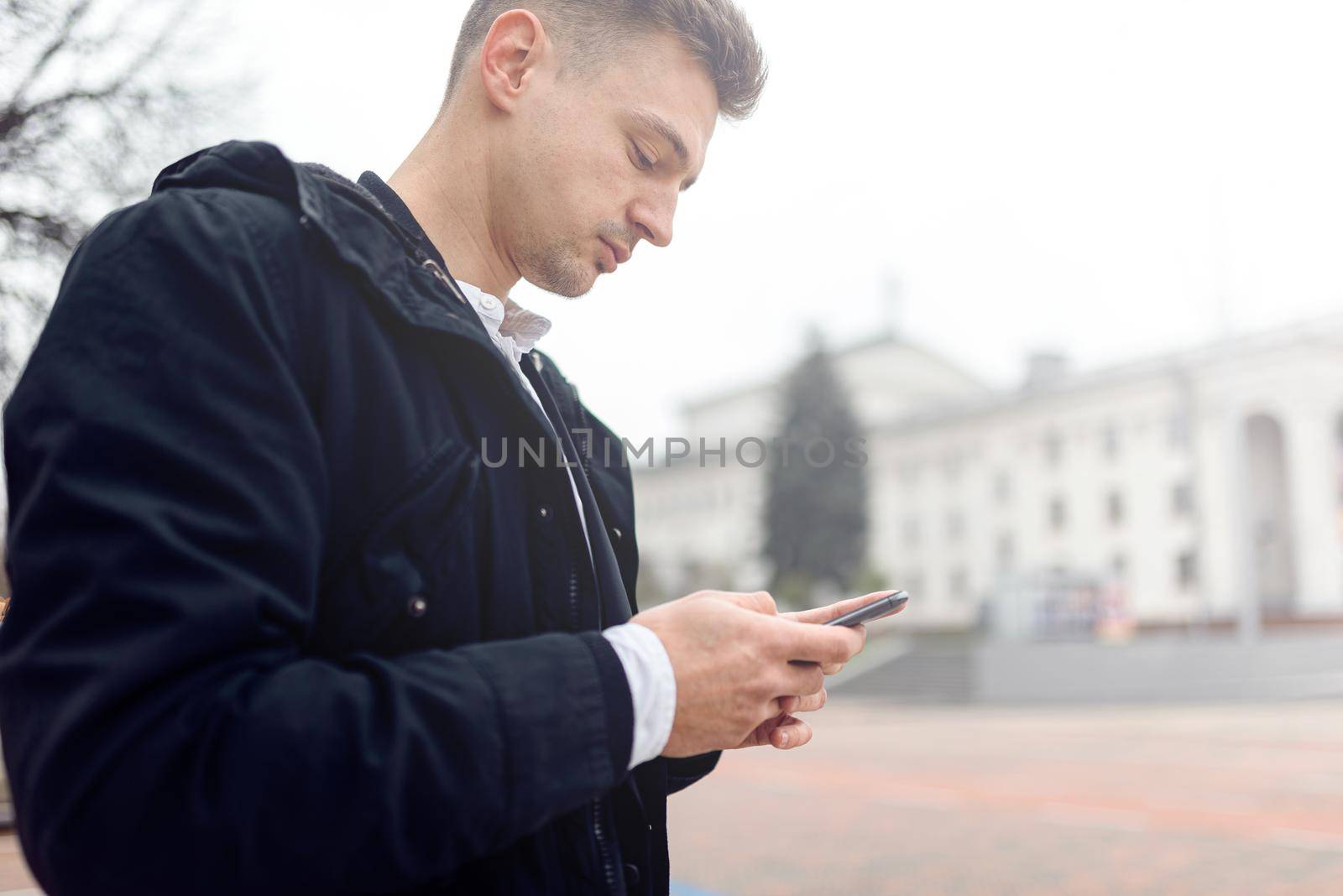 Young man typing on phone on the street by monakoartstudio