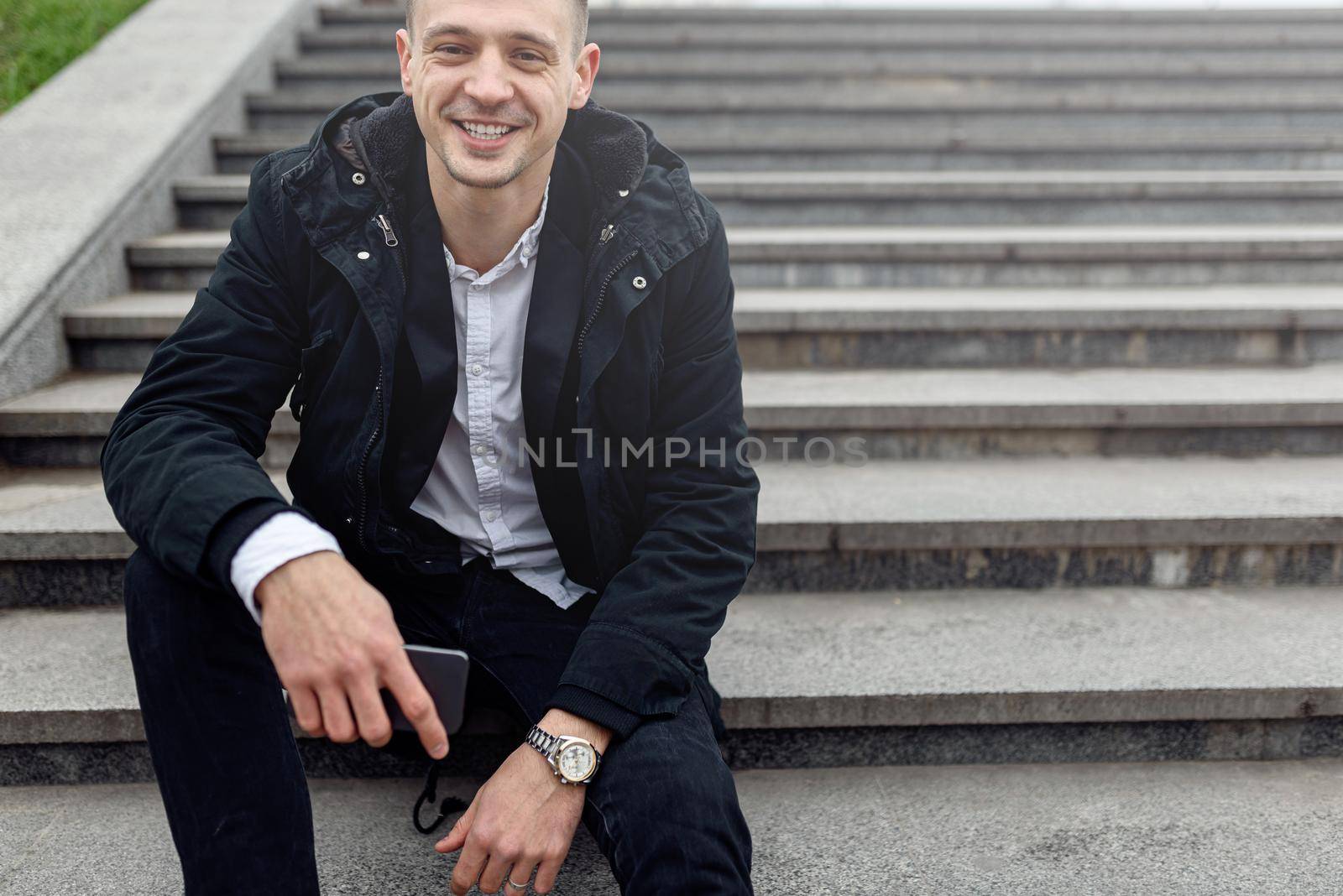 Cropped photo of smiling handsome young man enjoying day on the stairs on the street. Copy space. Lifestyle concept