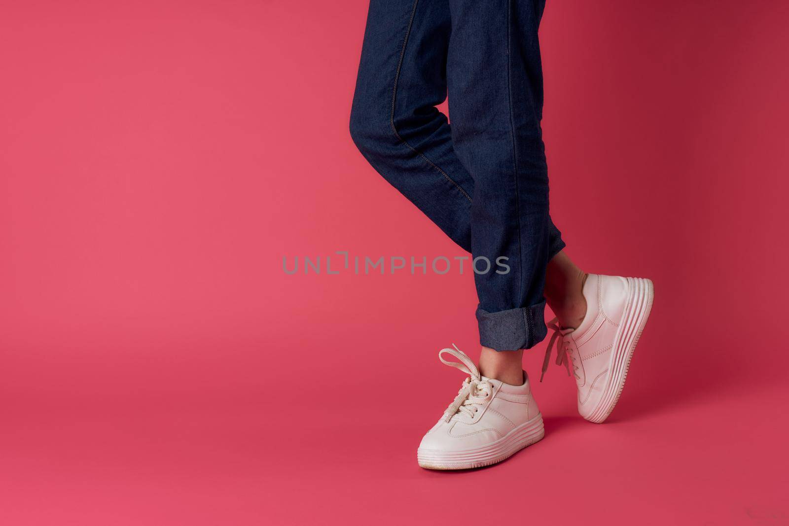 Female feet white sneakers street fashion pink background. High quality photo