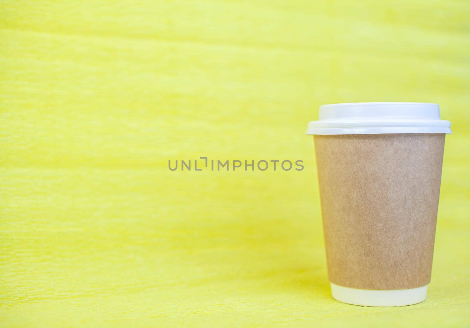 Paper cup of coffee closed with a white lid on a yellow background. There is a place for the text.