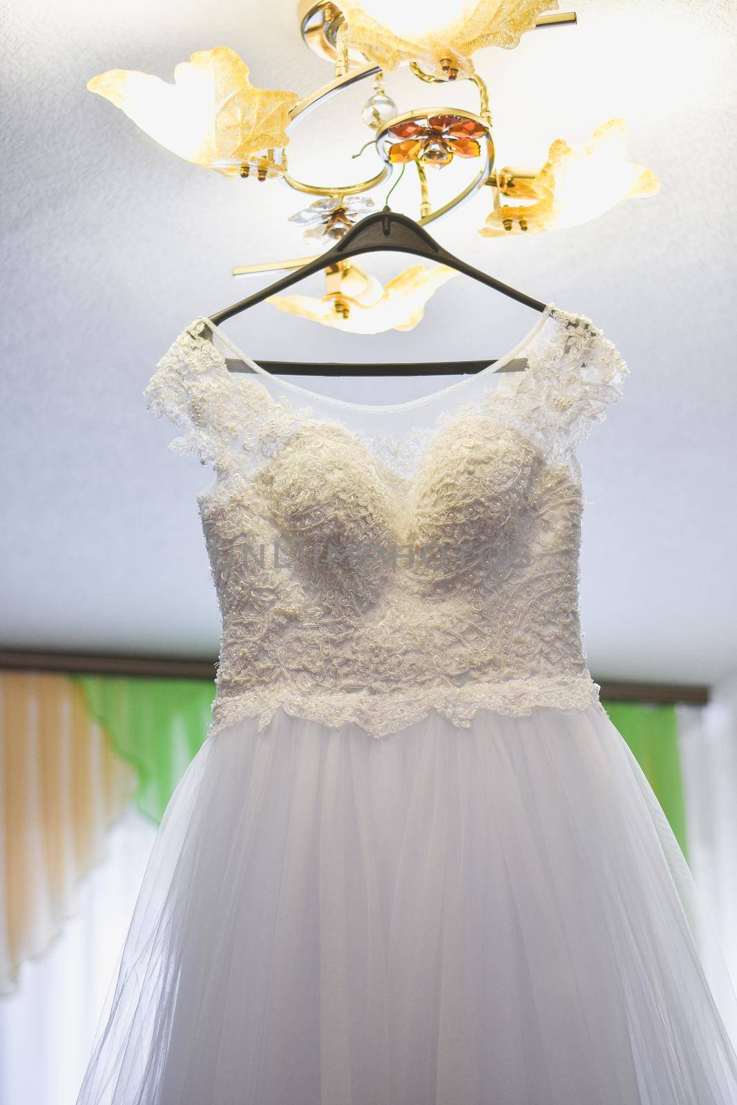The wedding dress hangs on the chandelier. In the home environment. Without people. Vertical photo.