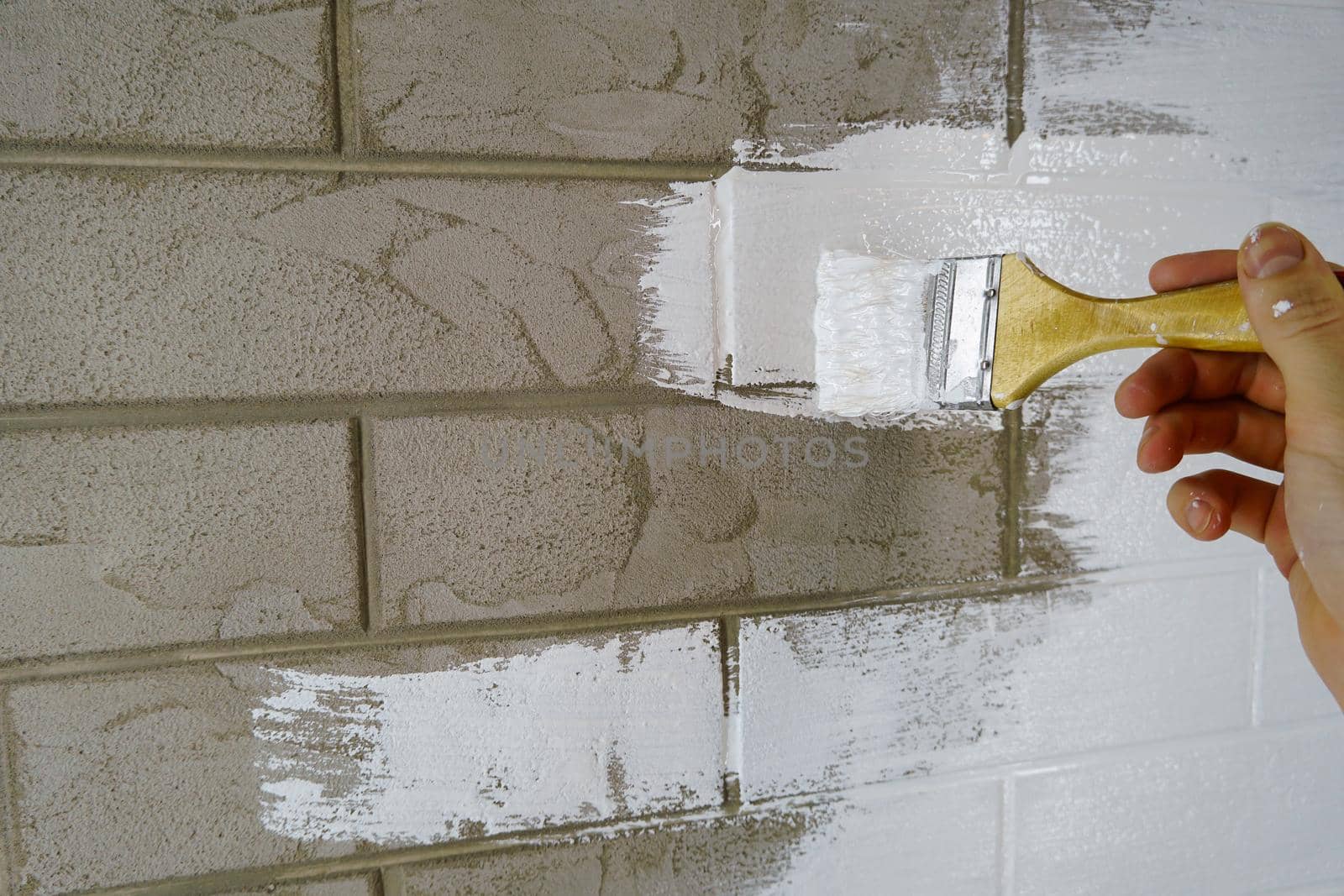 A construction worker applies paint to a brick wall.The painter paints primers the walls with a brush, makes repairs in the house or room.Reconstruction of the building, specialist restores the wall                                
