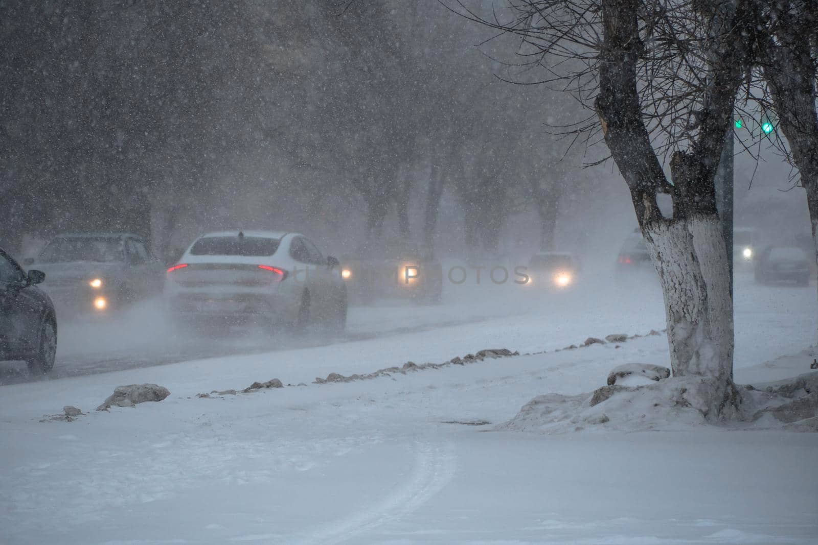 Snow-covered road with cars in a storm,blizzard or snowfall in winter in bad weather in the city.Extreme winter weather conditions in the north.Cars drive through the snow-covered streets of the city by YevgeniySam
