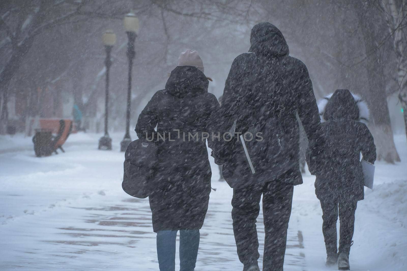 A snow-covered road with people in a storm,blizzard or snowfall in winter in bad weather in the city.Extreme winter weather conditions in the north.People walk through the streets under heavy snowfall by YevgeniySam