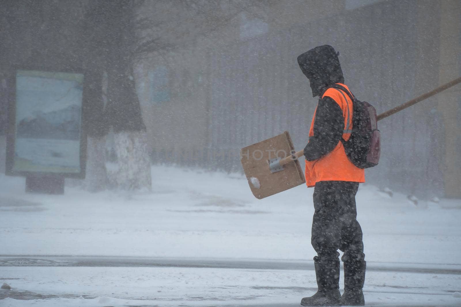 A working man of the municipal service with a snow shovel walks along the road in a storm, blizzard or snowfall in winter in bad weather in the city.Extreme winter weather conditions in the north.