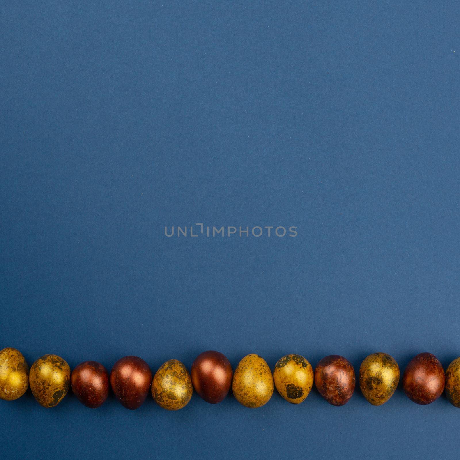 Small golden quail easter eggs in a row on blue background copy space for text