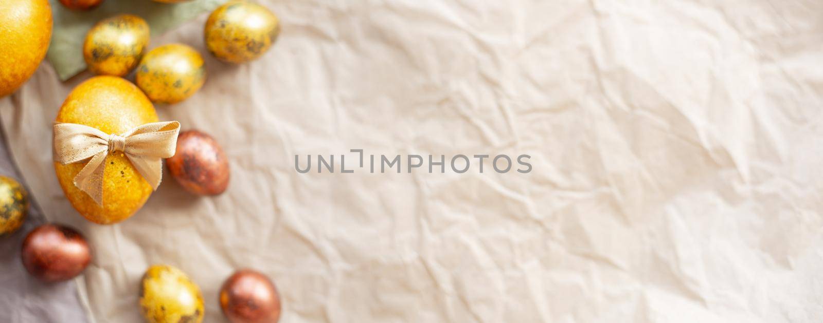 Golden easter eggs with ribbon bow on crumpled craft paper background copy space for text