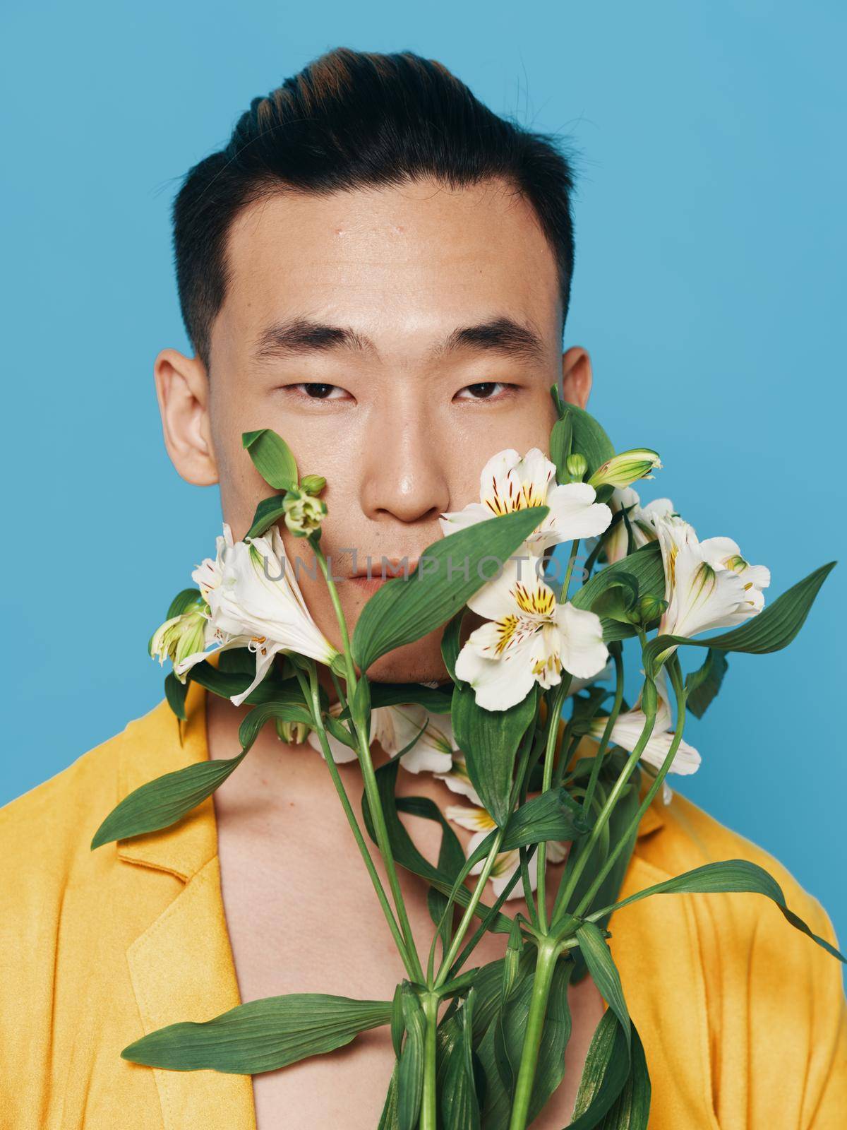 romantic asian guy with a bouquet of white flowers and in a yellow coat portrait . High quality photo