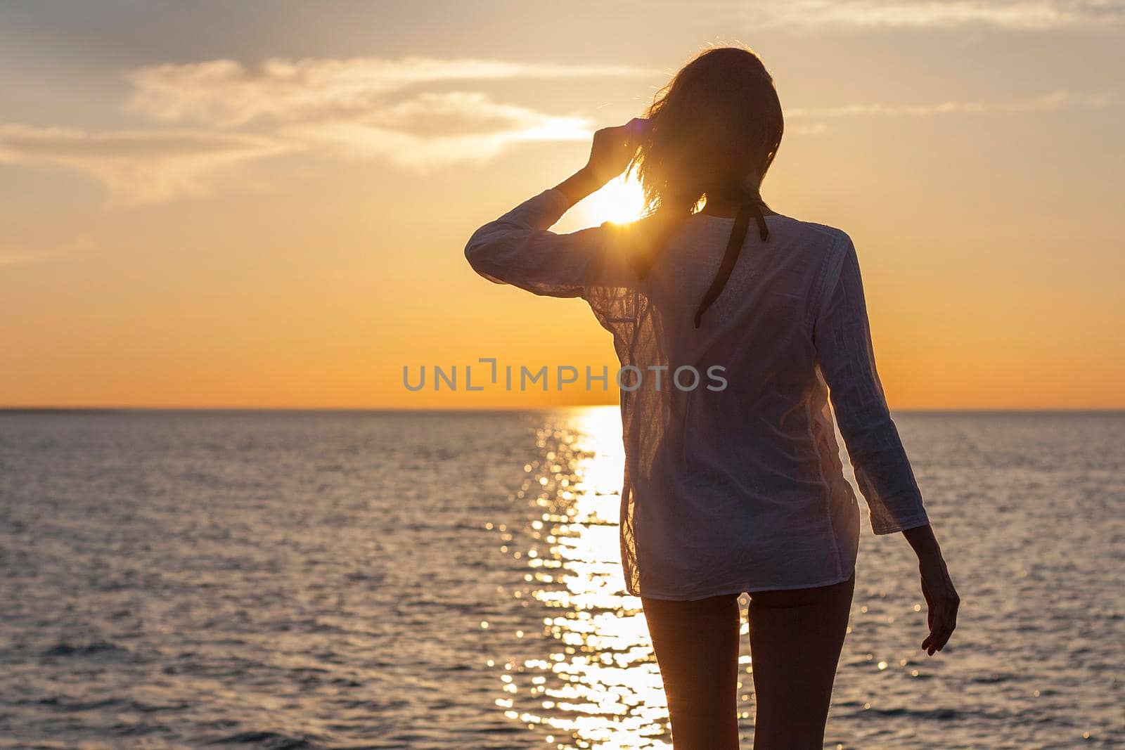 Silhouette of young happy carefree woman posing on the beach at sunset
