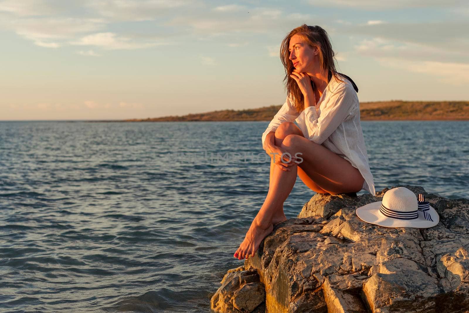 Beautiful woman enjoying sunset on the beach, sitting on rocks