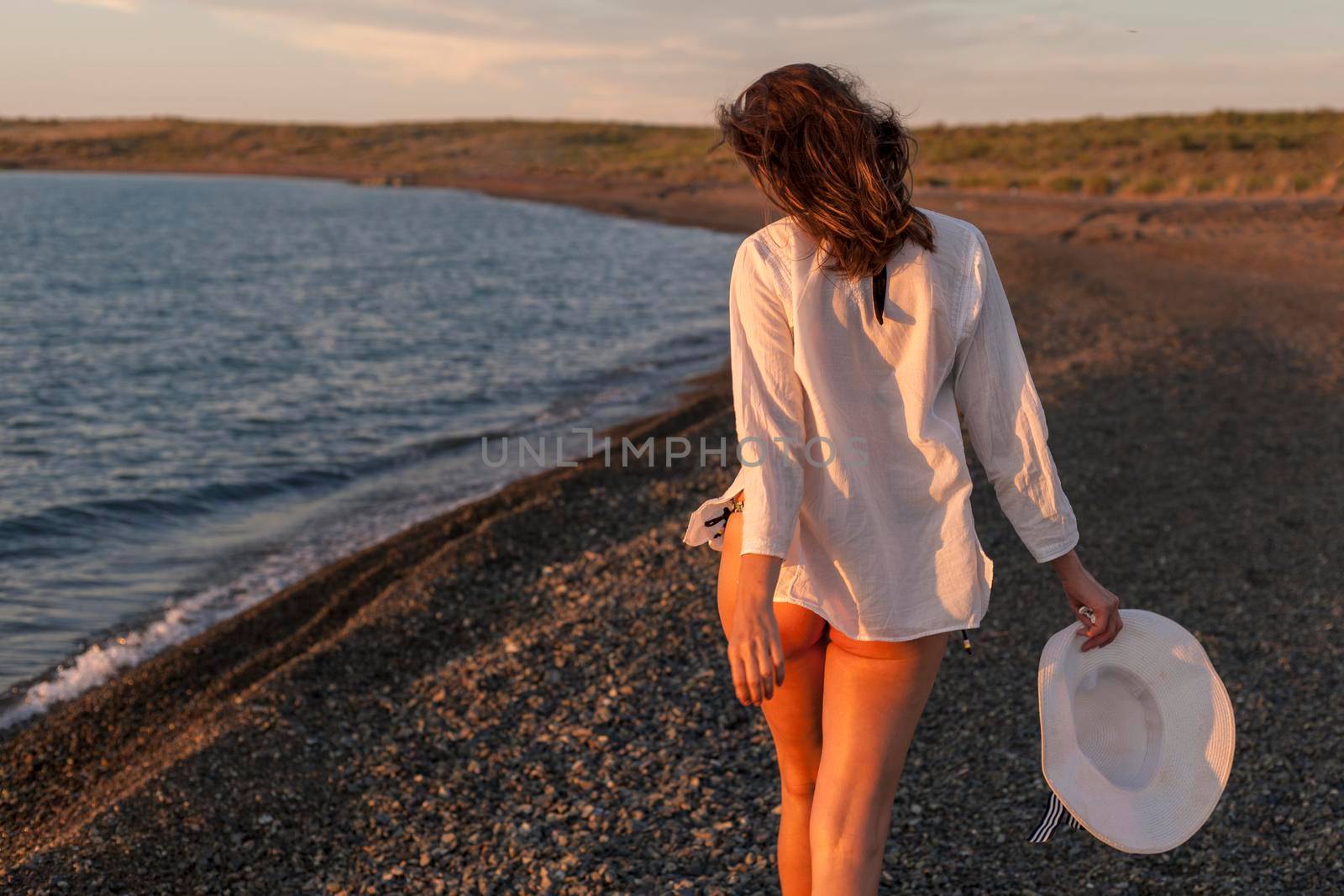 Woman walking on rocky beach with hat, rear view