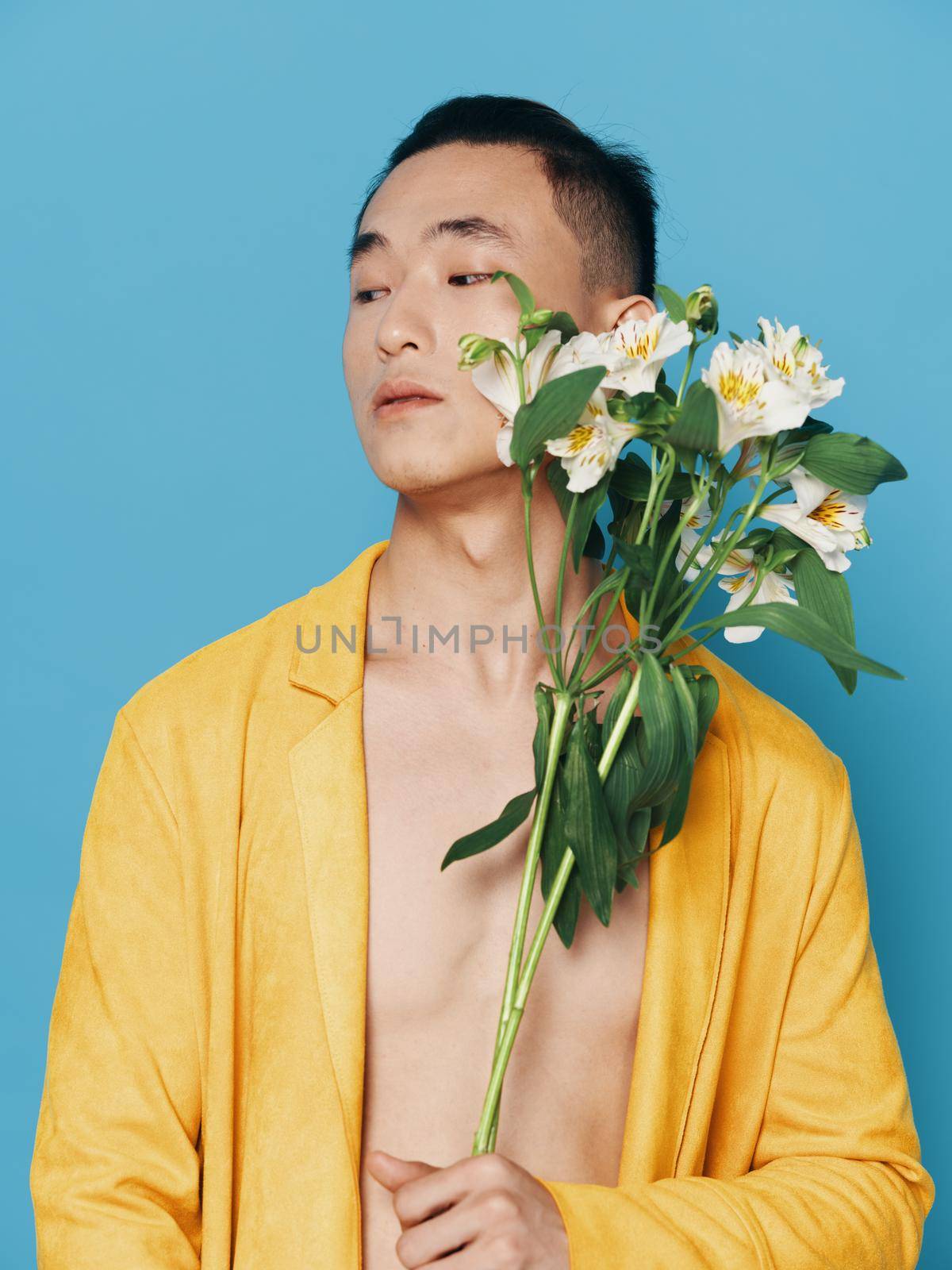 Cute Korean man in a yellow coat with a bouquet of white flowers on a blue background. High quality photo
