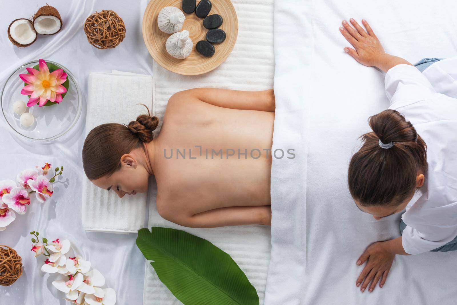 Woman at spa thai massage tow view, beauty treatments concept. Orchid and lotus flowers coconut stones and herb pouches