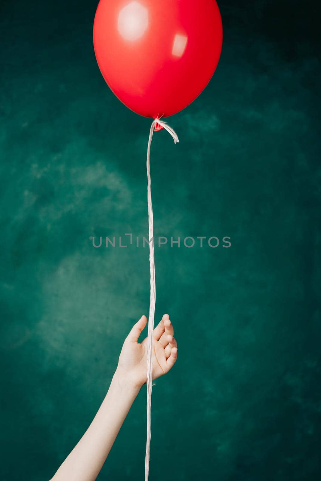 red balloon in hand on a green background flies up close-up. High quality photo