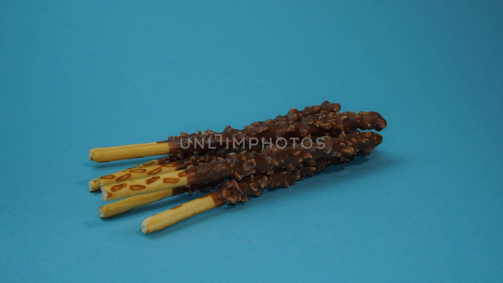 Chocolate crispy sticks with hazelnut sprinkles on a blue background.