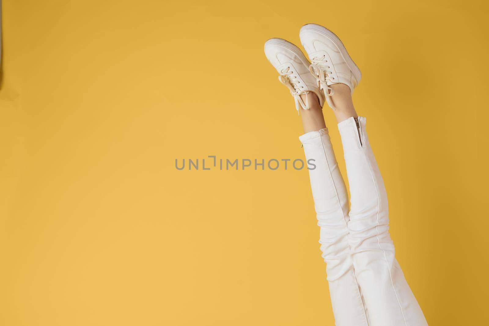 Female legs white jeans sneakers fashion yellow background view. High quality photo