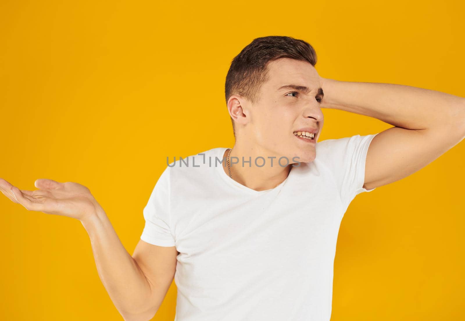 A guy in a white T-shirt spreads his arms to the sides on a yellow background emotions model by SHOTPRIME