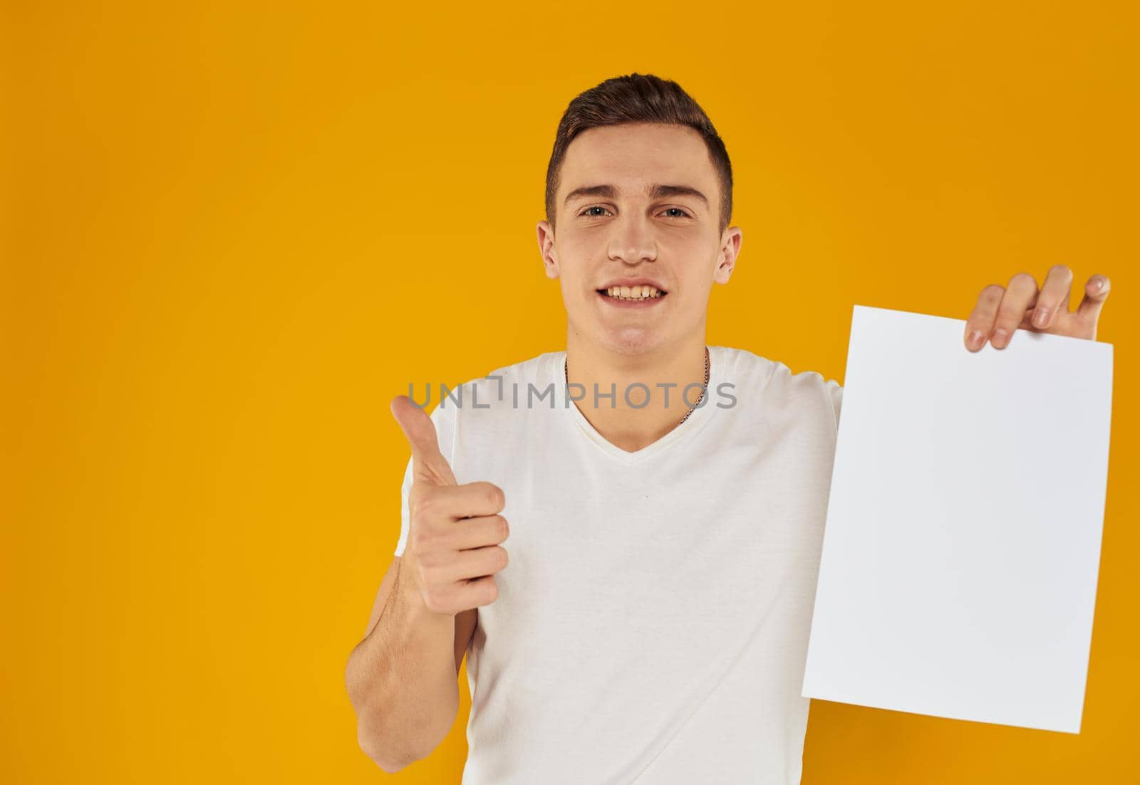 Guy with a white sheet of paper on a yellow background close-up cropped view by SHOTPRIME