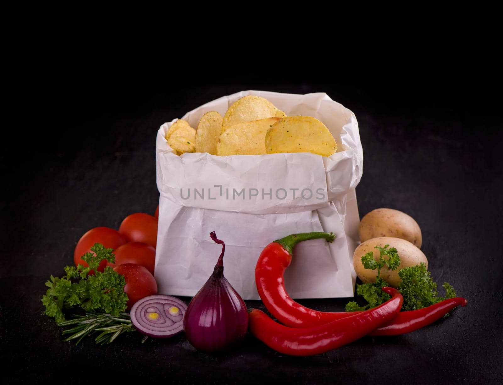 Crispy potato chips in a bag on dark table.