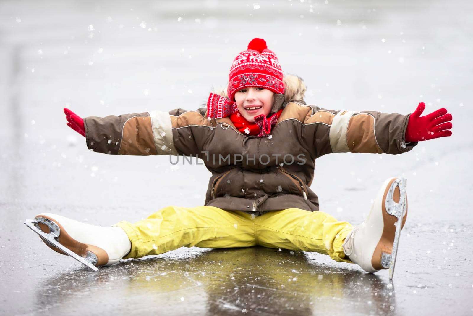 Little joyful boy fell down while skating. The child is skating on ice in the winter.
