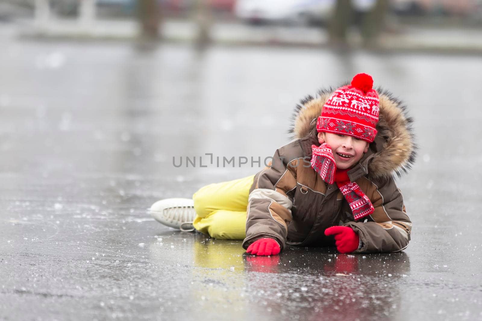 Funny boy fell down while skating. The child lies on the ice in the winter.