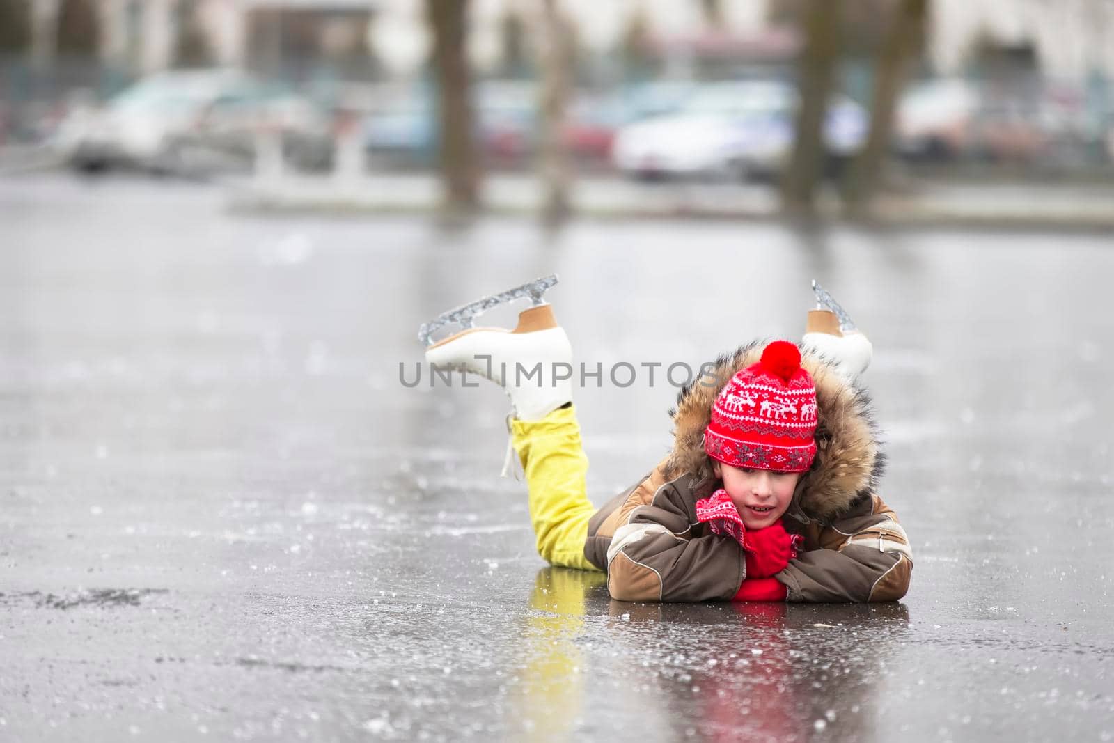 A boy in warm clothes and figure skates lies on the ice.