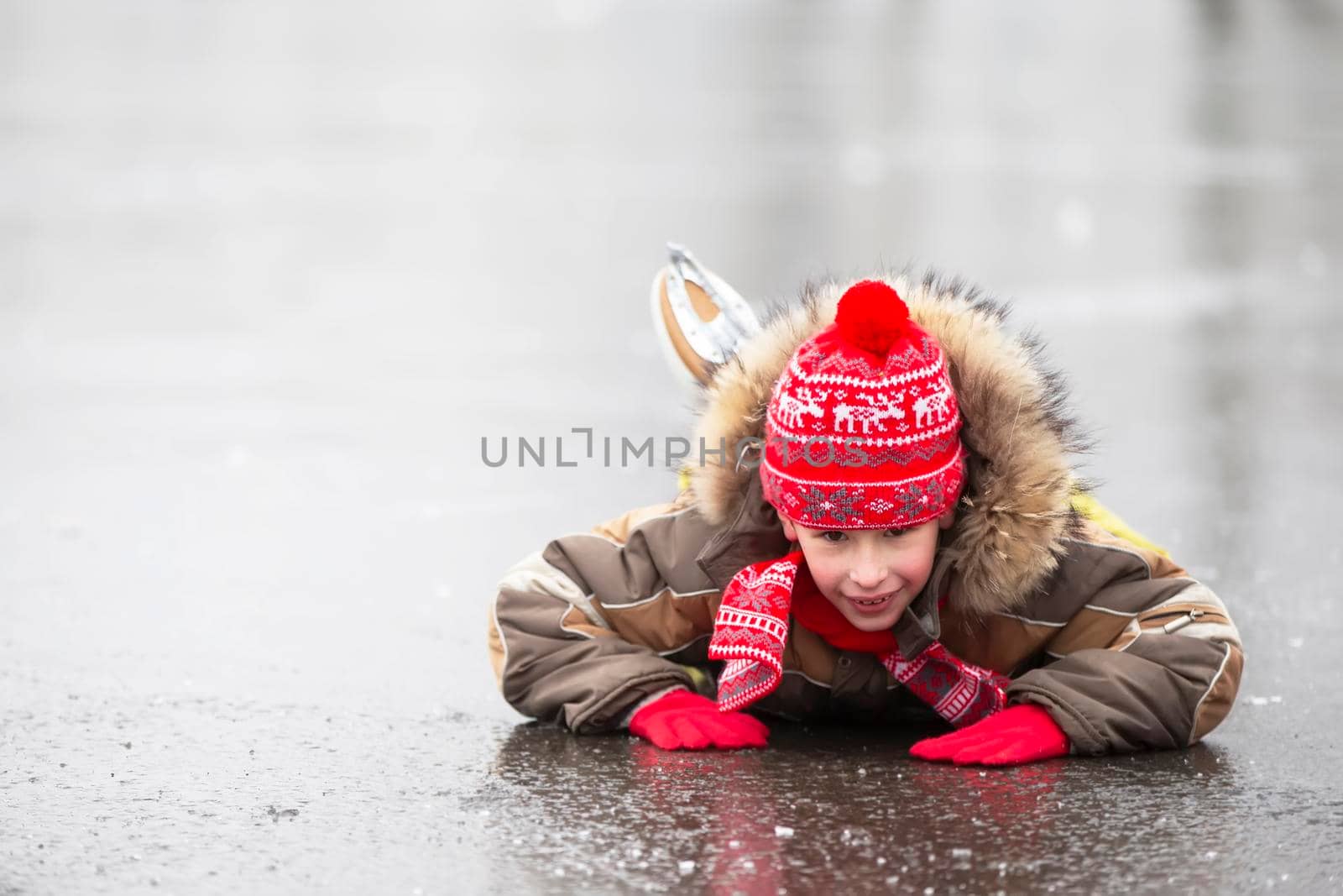 A boy in warm clothes and skates lies on the ice. and smiles.