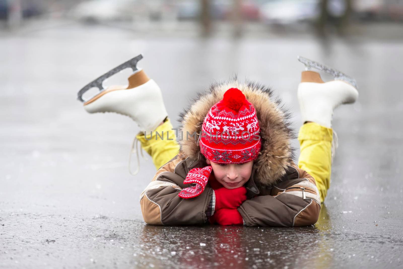 A child in figure skates in winter lies on the ice and smiles.